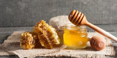 Med kapající z dřevěné naběračky na med, med v nádobě před dřevěným šedým pozadím