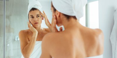 Žena si před zrcadlem vymačkává pupínky na tváři