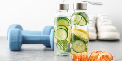 Voda s okurkami, citronem a máta ve dvou lahvích, v pozadí činky