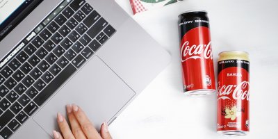 Dvě plechovky nápoje Coca-Cola ležící vedle notebooku