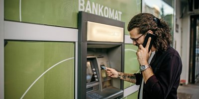 Telefonující muž si vybírá peníze z bankomatu
