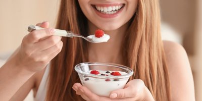 Usmívající se žena si nabírá jogurt s ovocem na lžičku