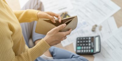 Žena drží prázdnou peněženku nad dokumenty s financemi