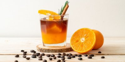 Sklenice ledové černé kávy americano a vrstva pomerančové a citronové šťávy zdobené rozmarýnem a skořicí na dřevěném pozadí