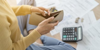 Žena s prázdnou peněženkou sedící nad papíry a kalkulačkou