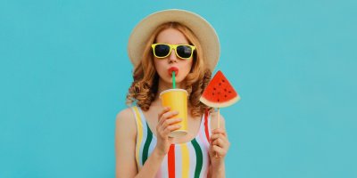 Žena ve slunečních brýlích pije z kelímku a drží meloun