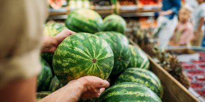 Muž vybírá z hromady melounů v supermarketu