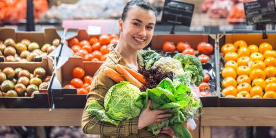 Žena v supermarketu s náručí plnou zeleniny